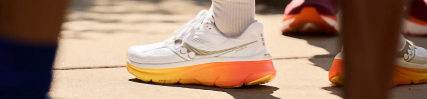 Close-up of a white Saucony running shoe with an orange-yellow gradient sole worn by a person.