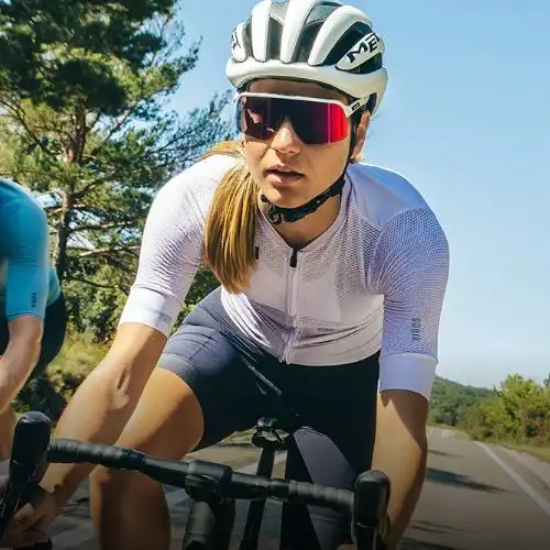 A female cyclist wearing a white jersey and helmet is riding on a road.