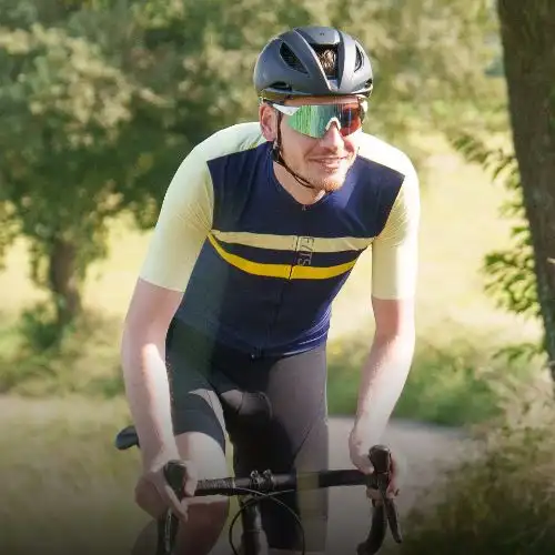 A cyclist wearing a blue and yellow jersey with a helmet and sunglasses, riding a bike outdoors.