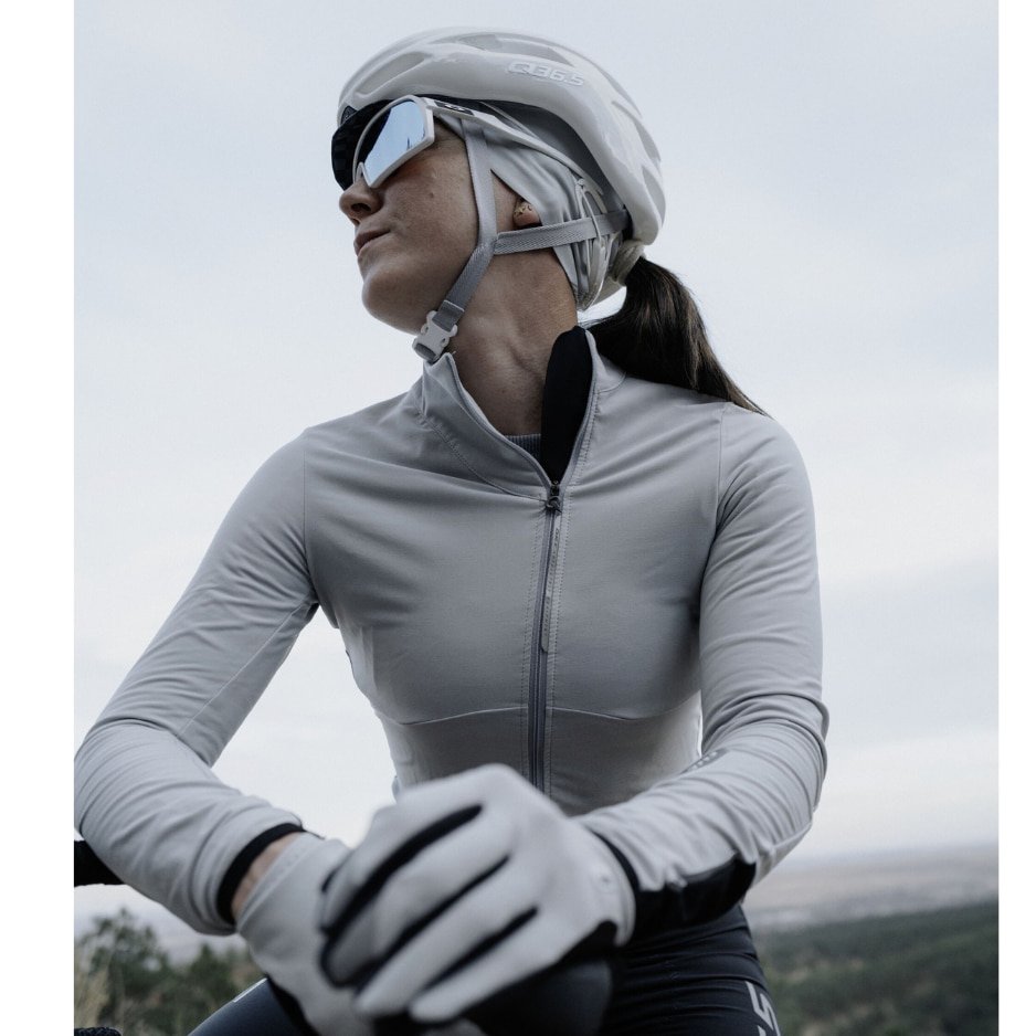 A cyclist wearing grey cycling gear and a white helmet, looking into the distance.