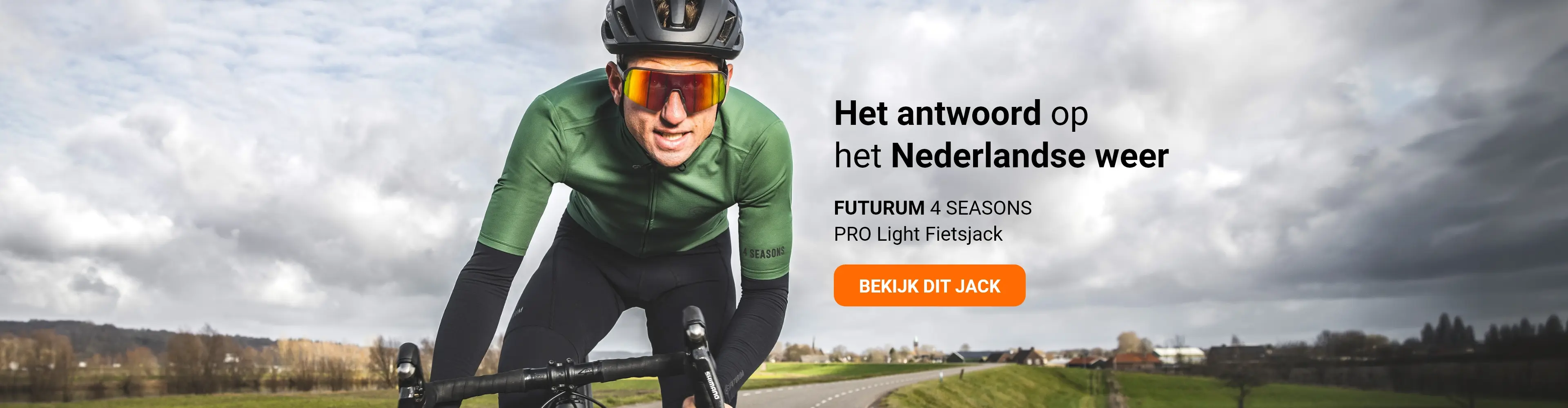 A cyclist wearing a green Futurum 4 Seasons Pro Light cycling jacket rides on a road under a cloudy sky.