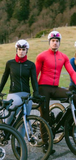 Een wielrenner met een bruine jas en een zwarte broek rijdt op een witte Canyon-racefiets.