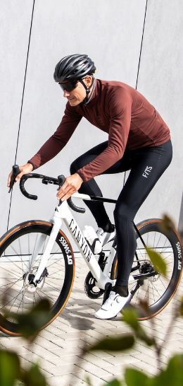 A cyclist wearing a brown jacket and black tights rides a white Canyon road bike.